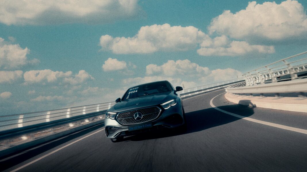 A stylish car navigates a curved highway under a bright, cloudy sky.
