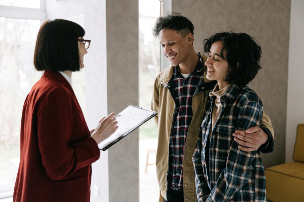 A young couple discusses housing options with a real estate agent inside a modern apartment.